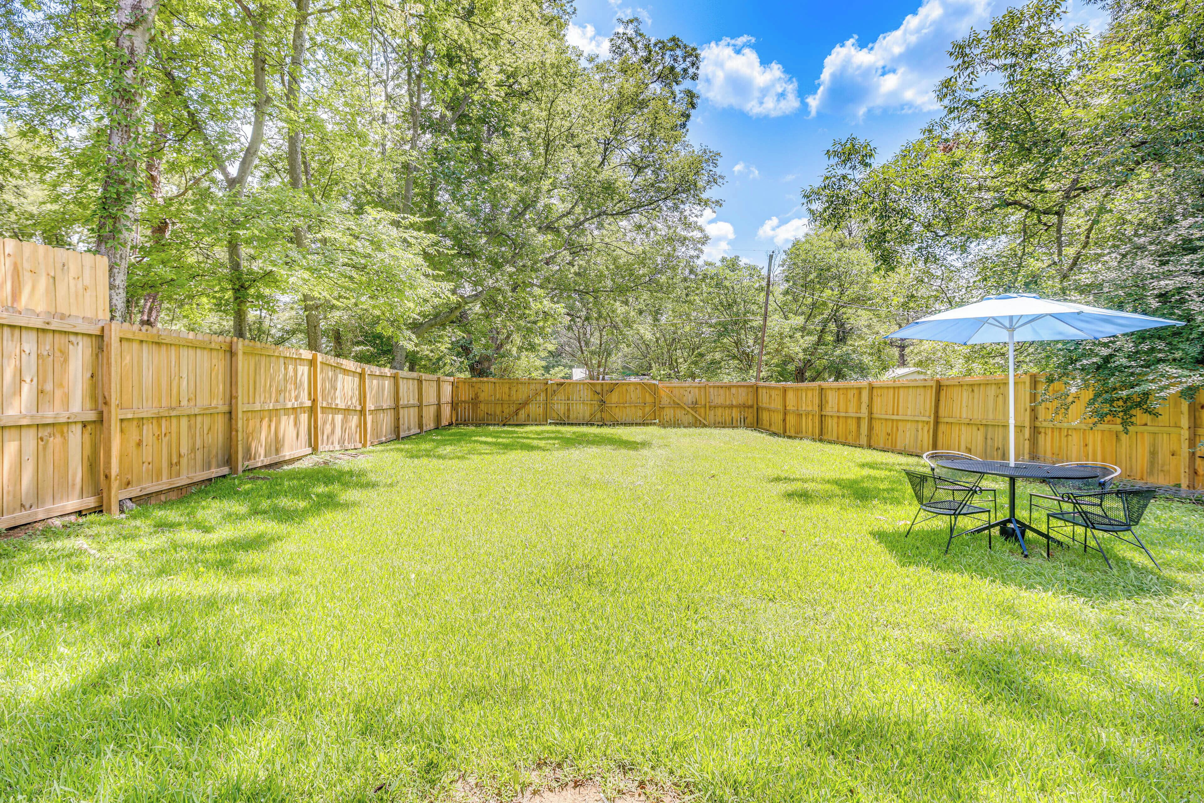 A backyard with a wooden fence, a grassy lawn, and a table with chairs under a blue umbrella.