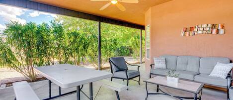 An outdoor patio with a table, chairs, a sofa, and a ceiling fan.