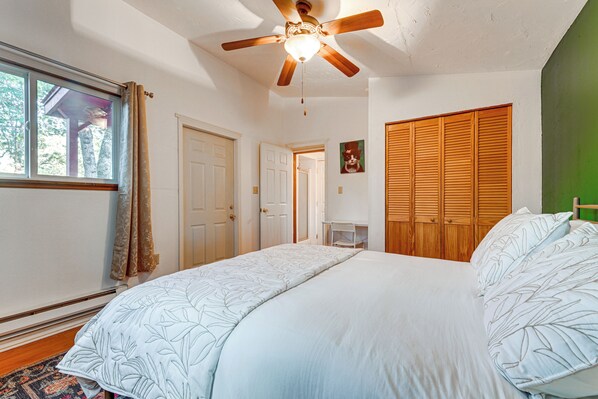 A bedroom with a large bed, a ceiling fan, a window with curtains, and a wooden wardrobe. - Grants Pass Cottage ~ 8 Mi to Rogue River! (Grants Pass)