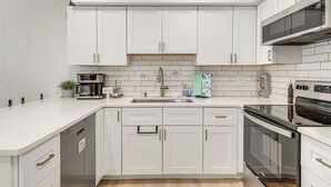A modern kitchen with white cabinetry, a stainless steel sink, a built-in oven, and a microwave.