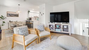 A modern living room with two wicker chairs, a television, and a dining area in the background.