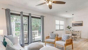 A spacious living room with a large sliding glass door leading to a patio, a ceiling fan, a dining area with a table and chairs, and a wall-mounted picture.