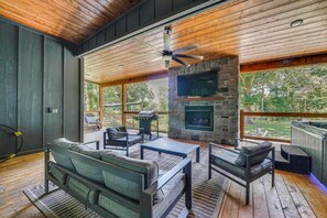 A spacious outdoor living area with a stone fireplace, comfortable seating, and a ceiling fan.