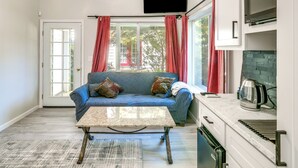 A living room with a blue sofa, a coffee table, and a kitchen area with a microwave and kettle.