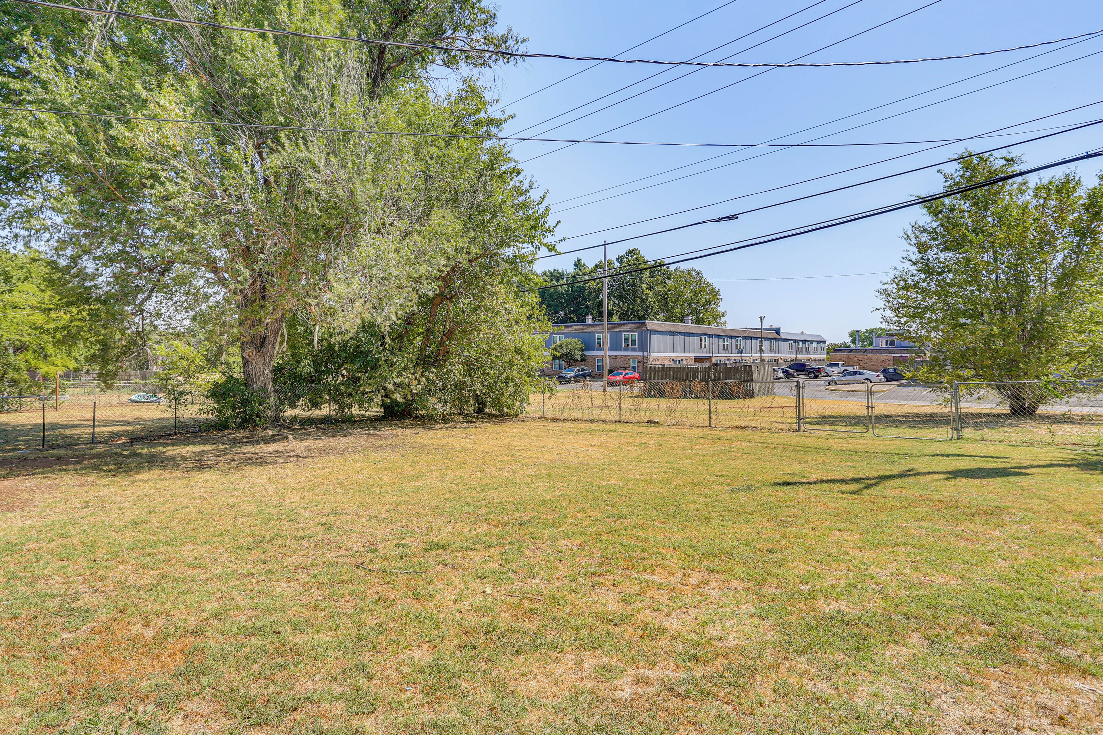 A fenced outdoor area with grass and trees, a building in the background, and power lines overhead.