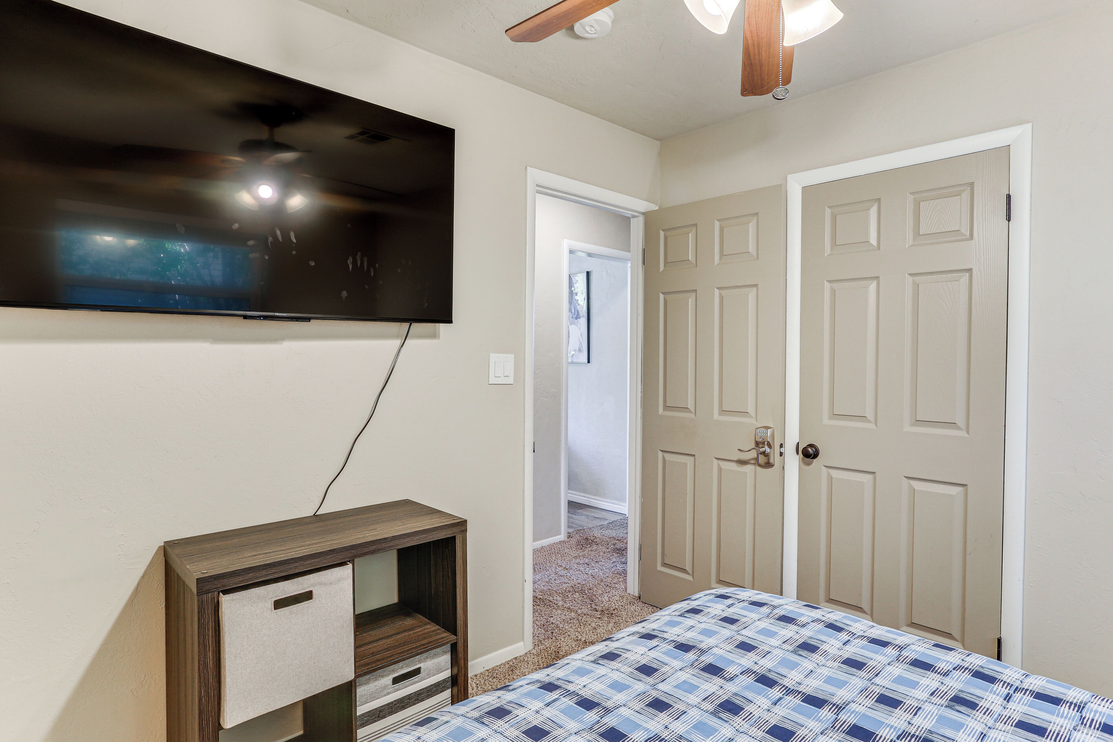 A bedroom with a bed, a TV mounted on the wall, and a door leading to another room.