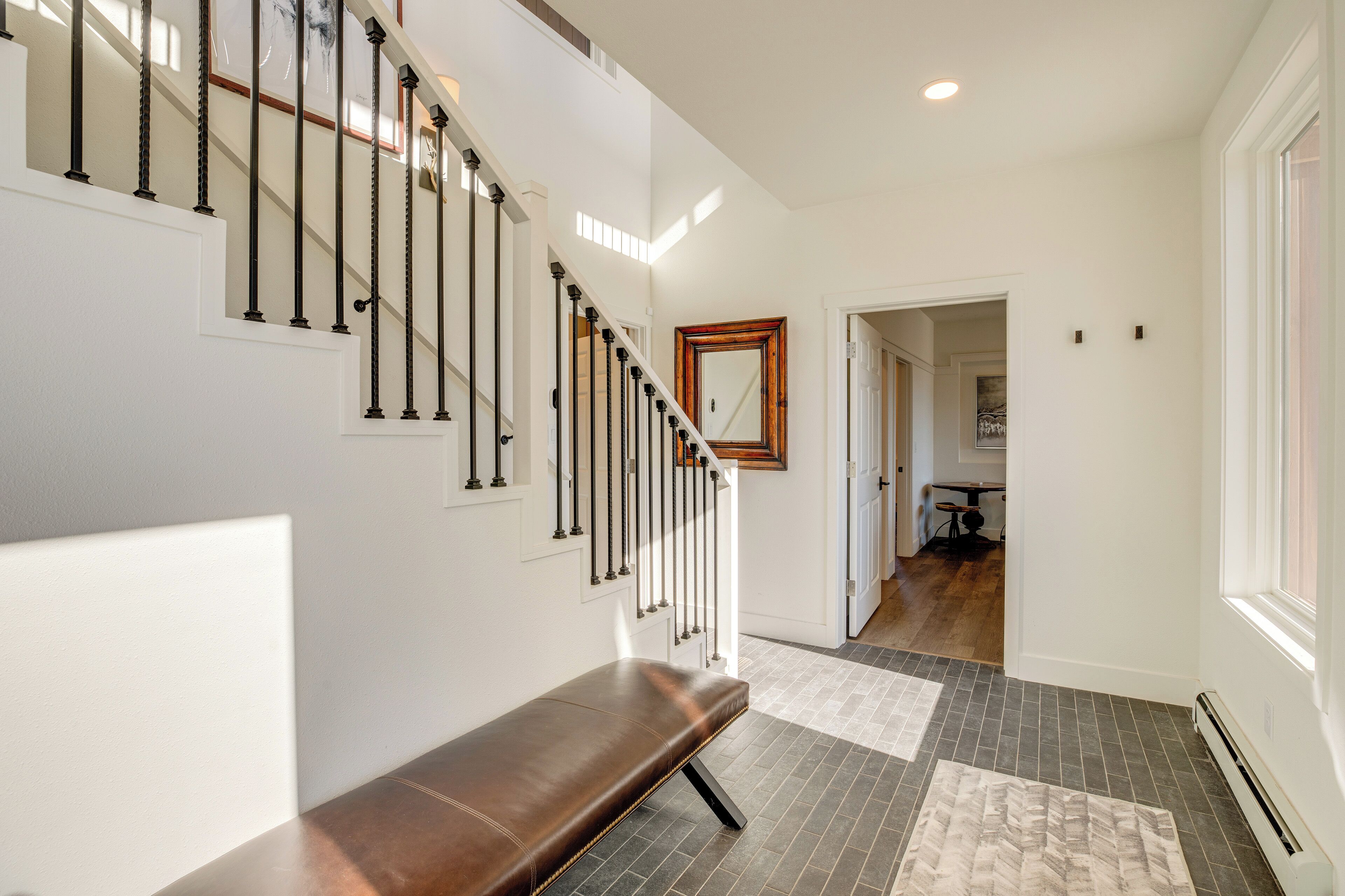 A staircase with black balusters, a bench, and a patterned rug on a tiled floor.