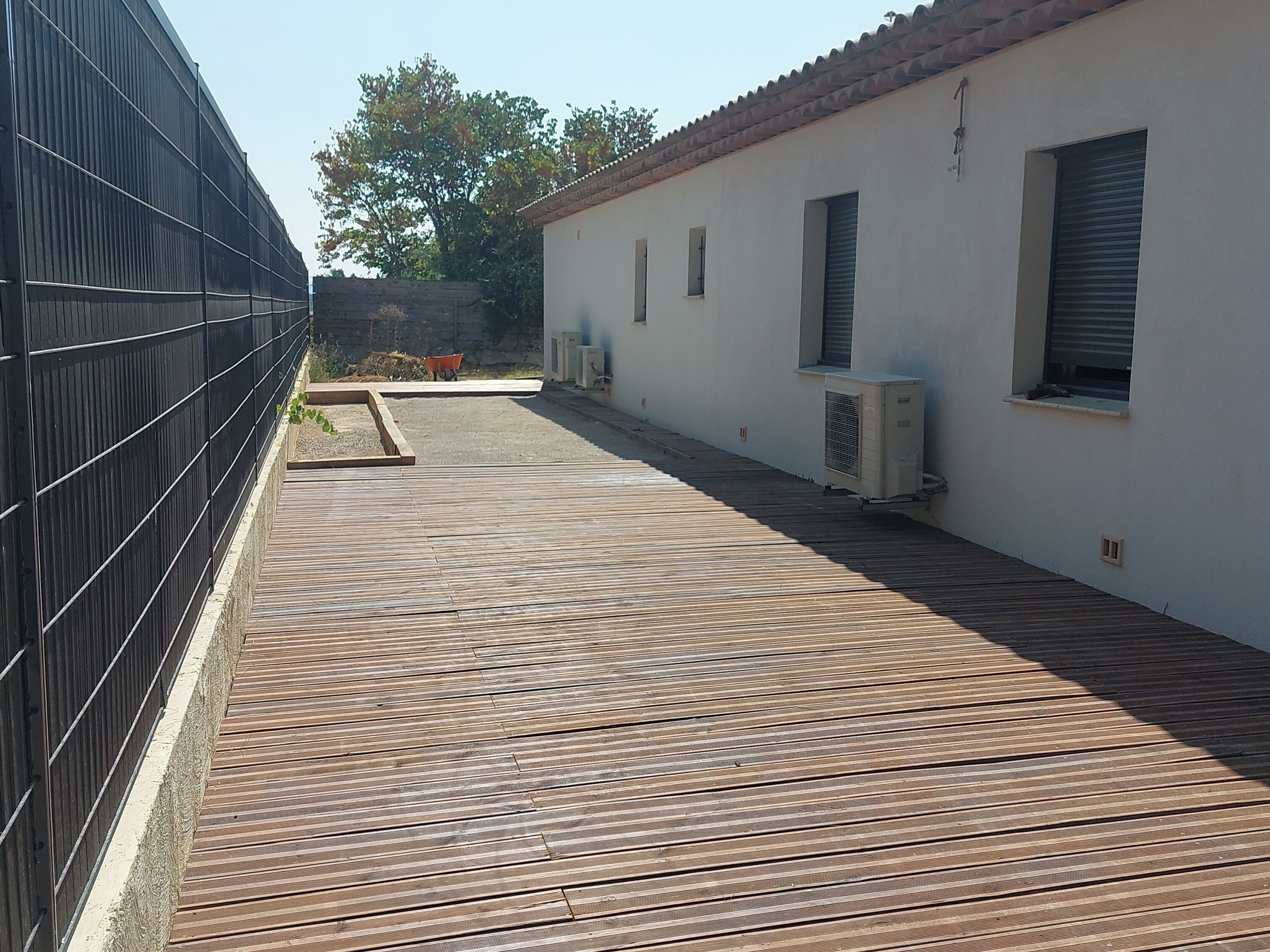 A rooftop with a wooden deck, air conditioning units, and a white building with windows.