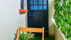 A narrow hallway with a black door, a small plant, and a wooden chair. - Lux Suites Three Unit Complex Ruiru (Ruiru)