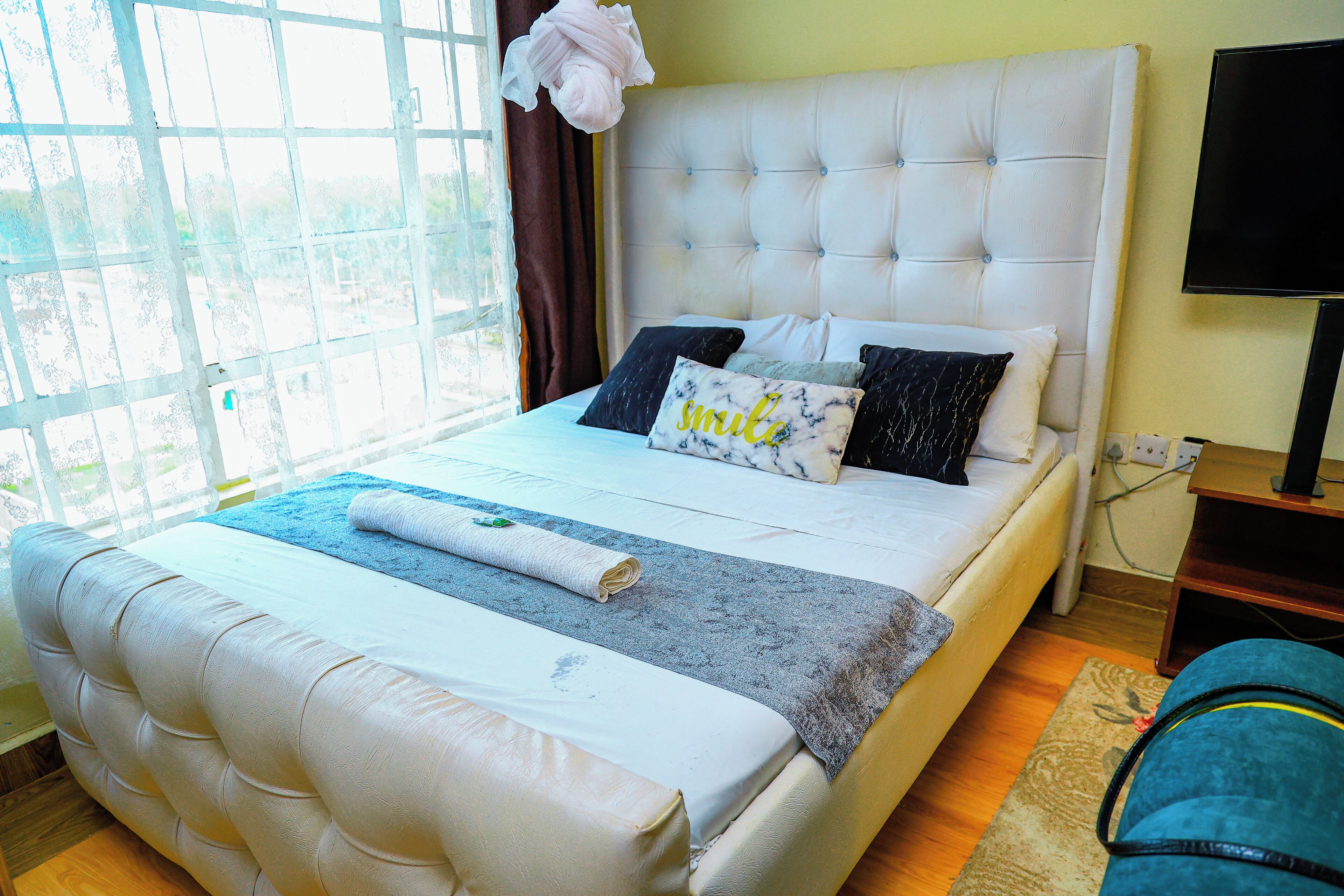 A neatly made bed with a grey and white bedspread, a rolled white towel, and two pillows with a marble design.