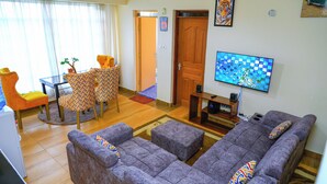 A living room with a sofa set, a television, and a dining area with chairs. - Lux Suites Three Unit Complex Ruiru (Ruiru)
