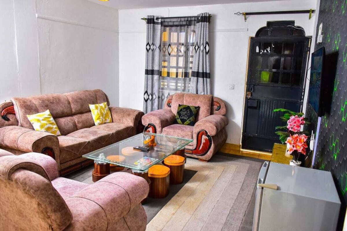 A living room with two pink sofas, a glass coffee table, and a small refrigerator.