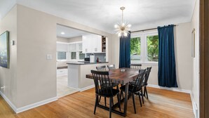 A modern kitchen with white cabinets, a wooden dining table with chairs, and a pendant light.