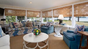 A sunroom with a view of a lake, furnished with blue sofas, a white table, and a decorative vase. - Minutes from Downtown St. Michaels | Pool | Cabana | Kayaks | Private Dock (St. Michaels)
