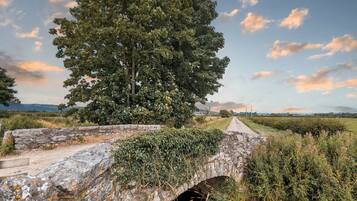 A rustic stone bridge with a tunnel underneath, surrounded by lush greenery and a clear sky.