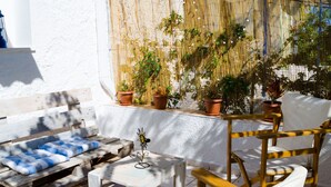A wooden outdoor seating area with a bench and a small table, surrounded by potted plants and a white wall. - Marini Traditional Cottages (Aegina)
