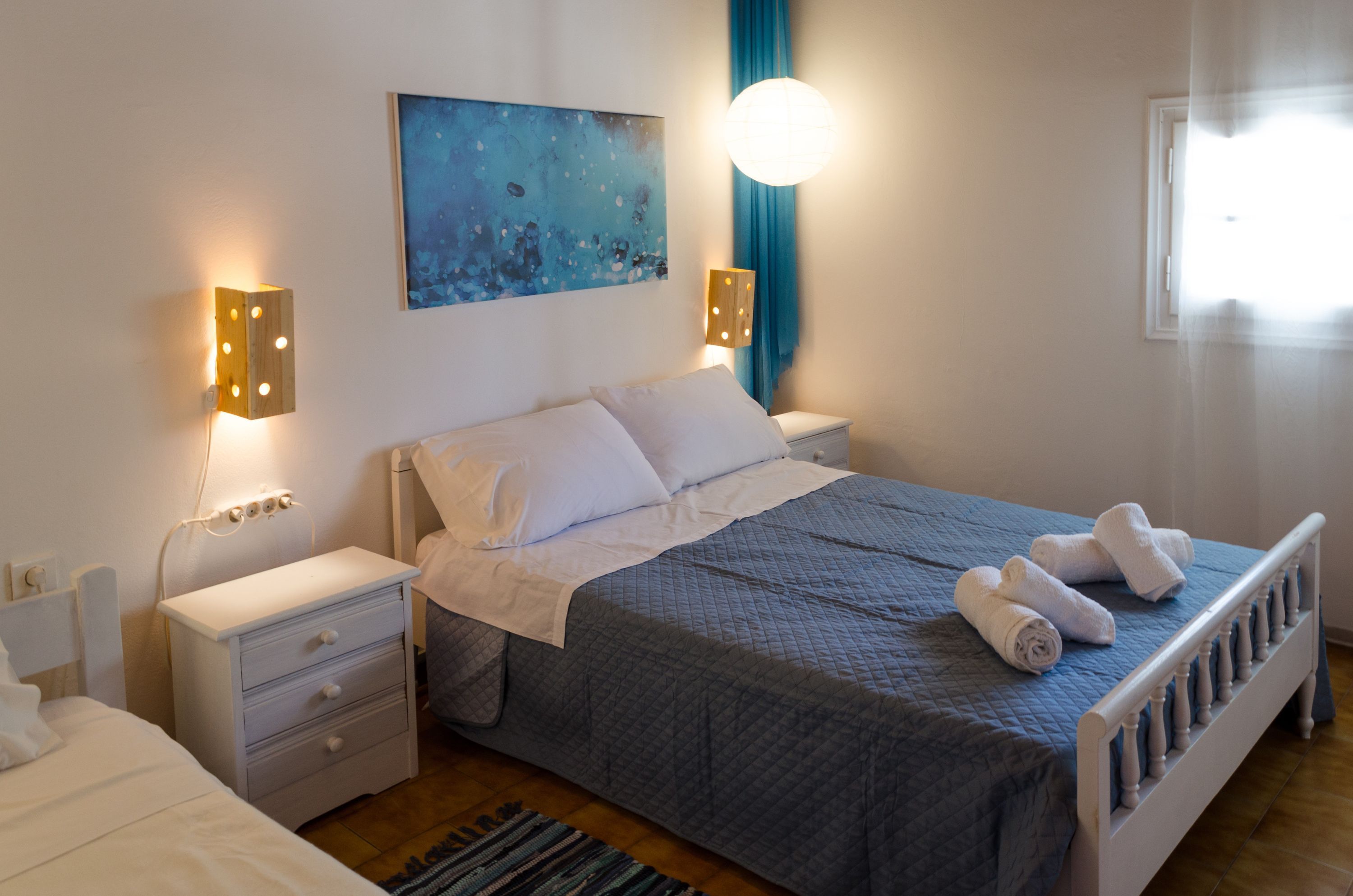 A bedroom with a bed, bedside tables, a nightstand, a wall-mounted lamp, and a painting.