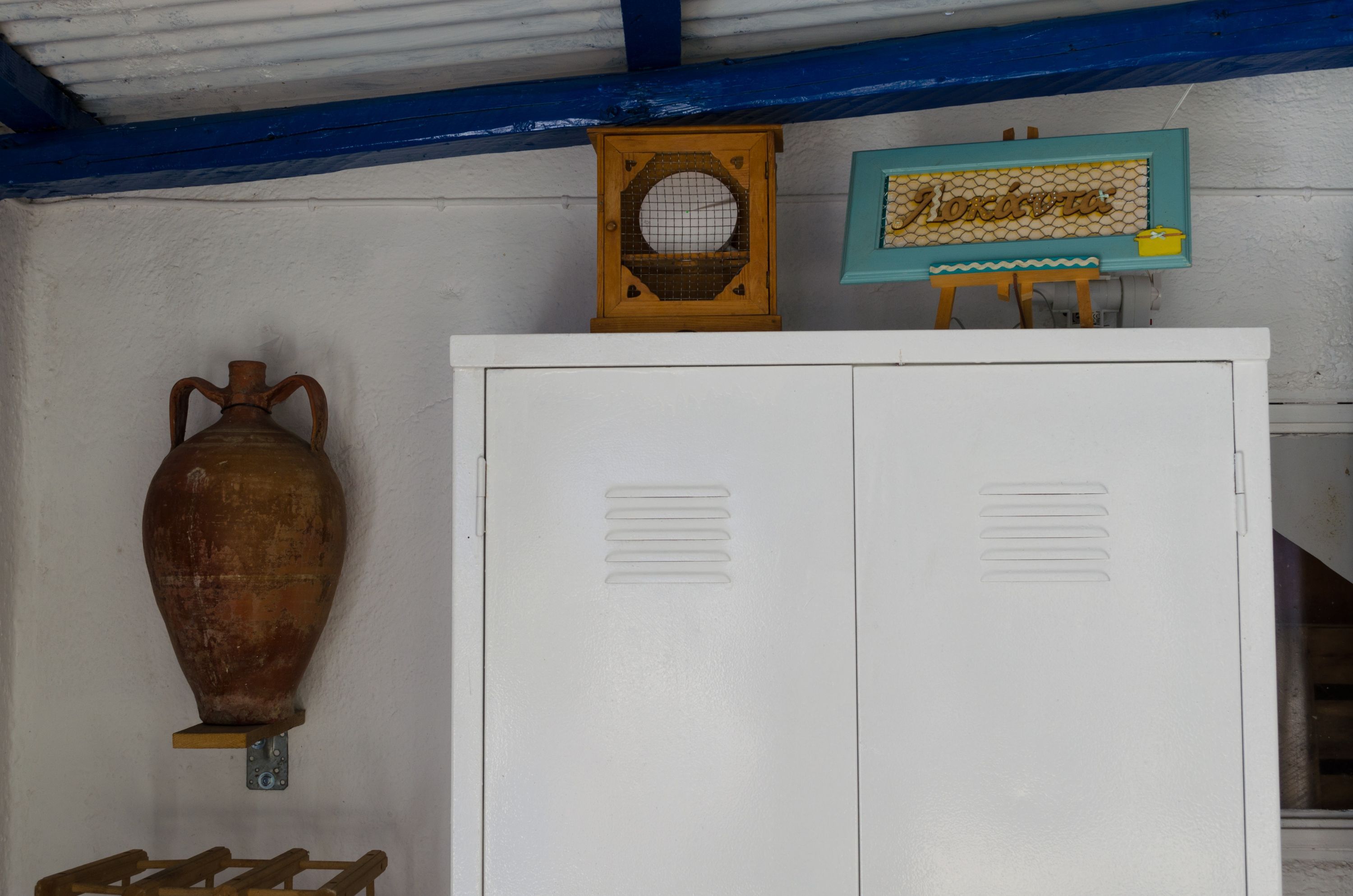 A white cabinet with ventilation slits, a wooden vase, and a sign with the name 'Mokodava'.