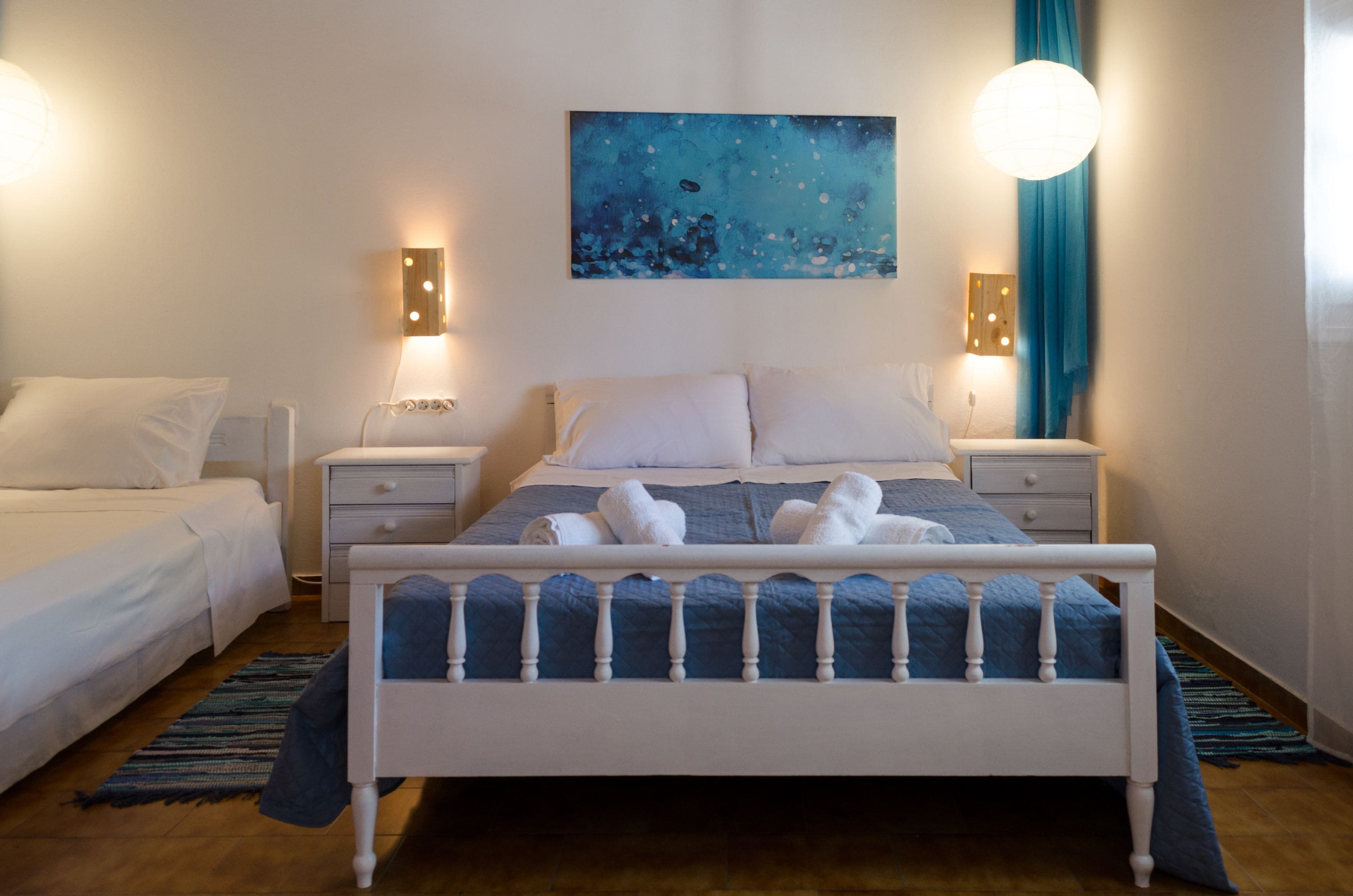 Ein Schlafzimmer mit einem Bett, zwei Nachttischen, einem Schreibtisch, einem Gemälde und einem Fenster mit Vorhängen.