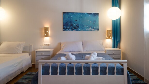 A bedroom with a bed, two bedside tables, a wall-mounted painting, and a window with curtains. - Marini Traditional Cottages (Aegina)