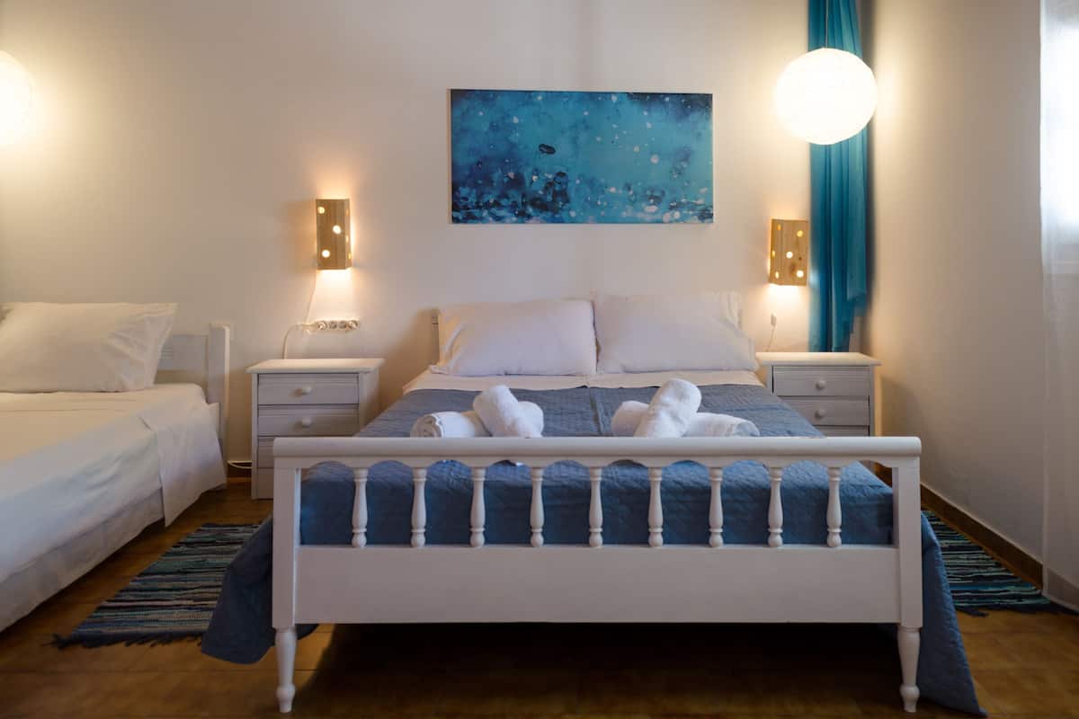 A bedroom with a bed, two bedside tables, a wall-mounted painting, and a window with curtains.