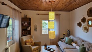 A cozy living room with a wooden ceiling, a bookshelf, a television, a sofa, and a coffee table. - Marini Traditional Cottages (Aegina)