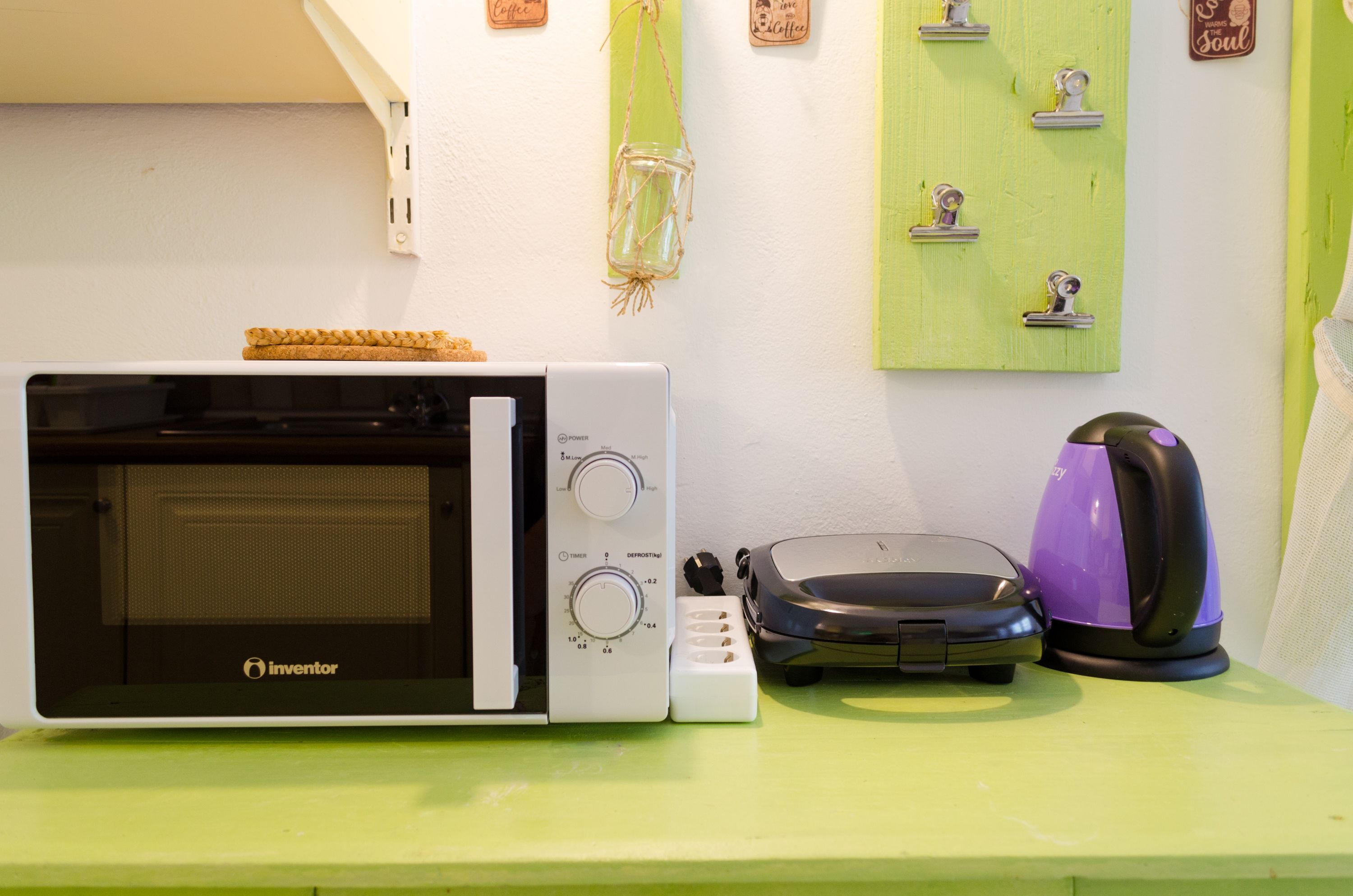 Une cuisine équipée d’un four à micro-ondes, d’un grille-pain et d’une bouilloire, le tout posé sur un plan de travail vert.