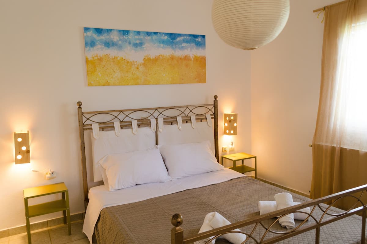 A neatly made bed with white linens, a painting above it, and bedside lamps on nightstands.