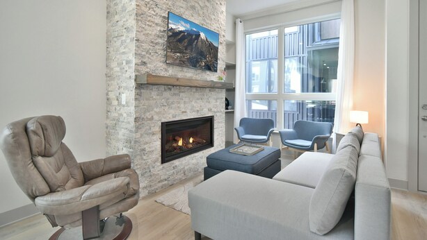Una sala de estar con chimenea de piedra, un sofá cómodo, un sillón reclinable y un ventanal grande.