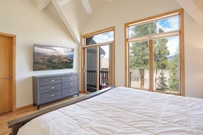 Un dormitorio con una cama grande, un tocador, un televisor y un balcón con vistas a árboles y montañas.