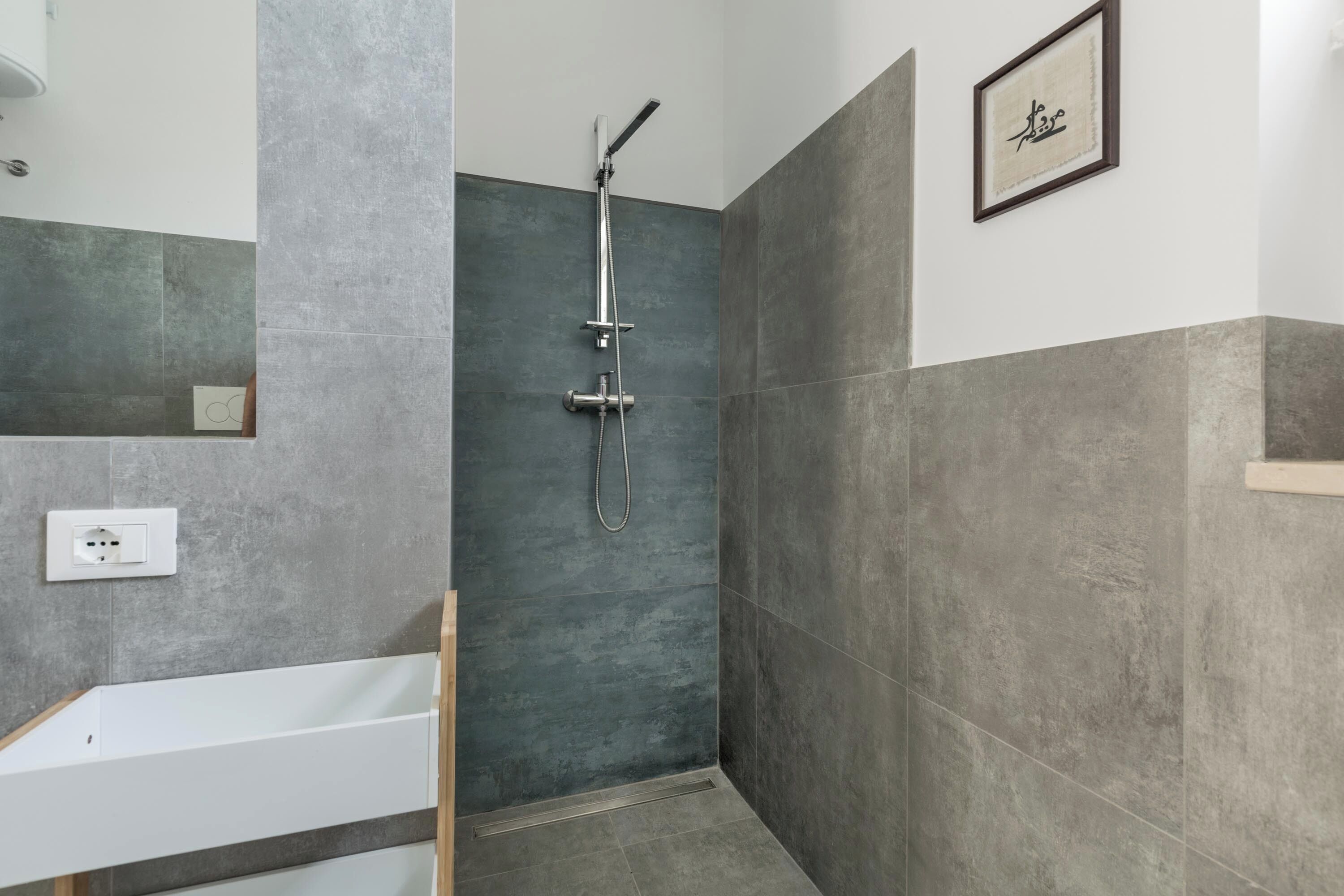 Une salle de bain moderne avec une douche, une baignoire blanche et une prise électrique fixée au mur.