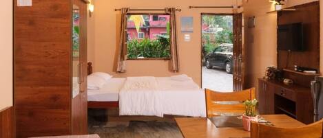 Una habitación con cama, escritorio y televisión. Hay una ventana con cortinas y una puerta que da al exterior.