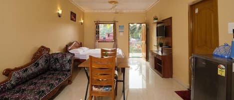 A room with a sofa, dining table, chairs, a refrigerator, and a television.