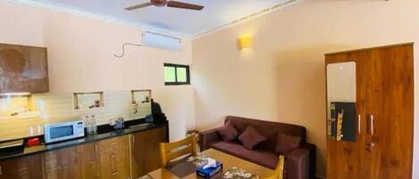 A compact living space with a kitchenette, a dining area, a sofa, and a wooden door.