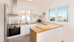 A modern kitchen with white cabinetry, a stainless steel refrigerator, and a wooden countertop. - Olive Leaf Kastela - First Floor Apartment (Kastela)