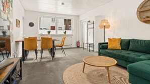 A modern living room with a green sofa, a round coffee table, and a dining area with a table and chairs. - Kamingo for 12 people - Central, terrace, PS4 & Stream (Frankenberg (Eder))