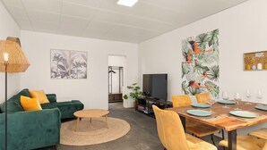 A modern living room with a green sofa, yellow cushions, a round coffee table, and a dining area with yellow chairs and a wooden table set for four. - Kamingo for 12 people - Central, terrace, PS4 & Stream (Frankenberg (Eder))