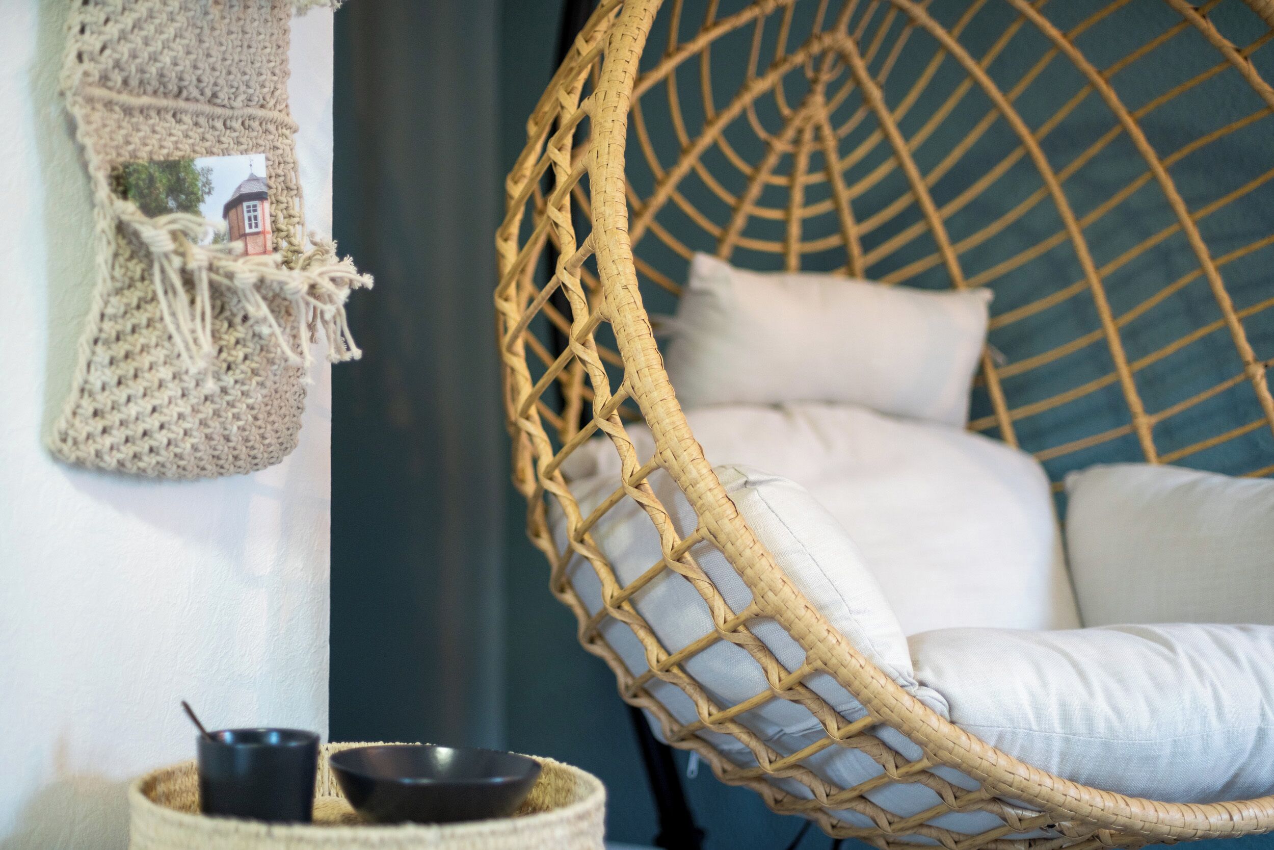 A wicker chair with a cushion, a woven wall hanging, and a small basket with bowls.