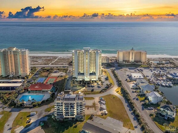 An aerial view of a coastal hotel complex with multiple high-rise buildings, a marina, and a swimming pool.