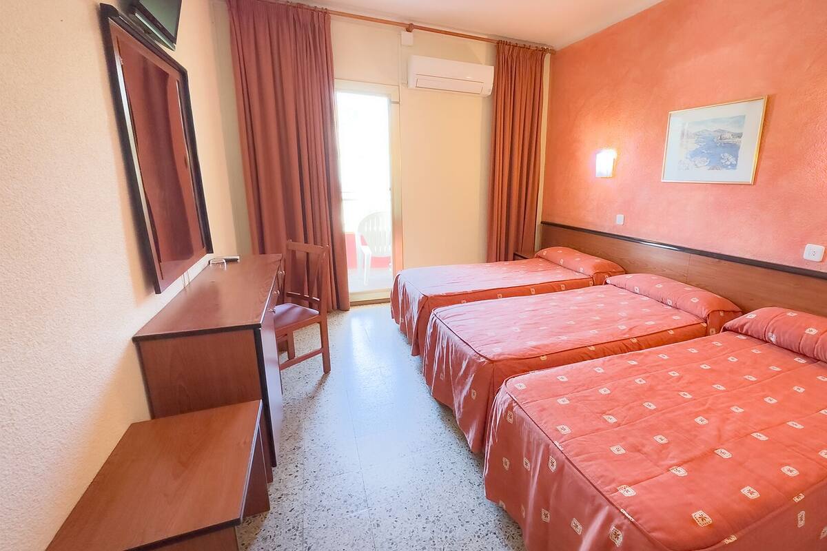 A hotel room with two beds, a desk, a chair, an air conditioning unit, and a window with curtains.