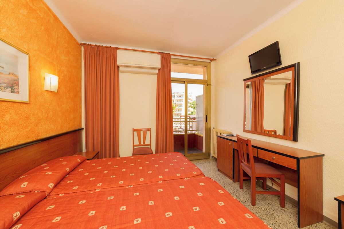 A hotel room with a bed, a desk, a chair, a television, and a window with curtains.