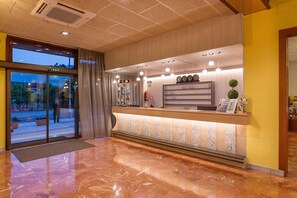 A hotel reception area with a marble floor, a reception desk with a clock, and a view of the street outside. - BLUESEA Continental (Tossa de Mar)
