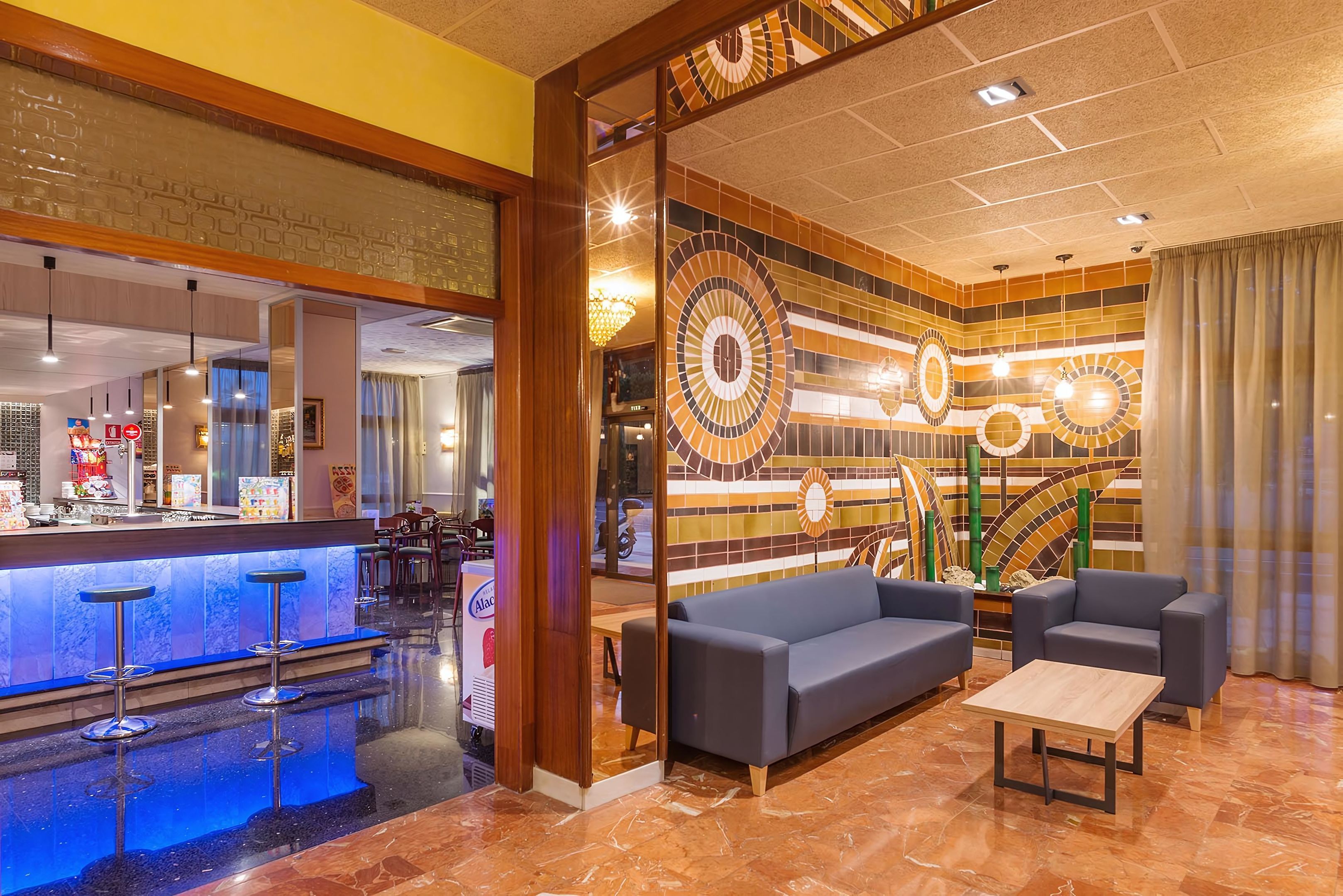 Un hall d’hôtel comprenant un bar, des espaces pour s’asseoir et un mur décoratif orné de motifs circulaires.