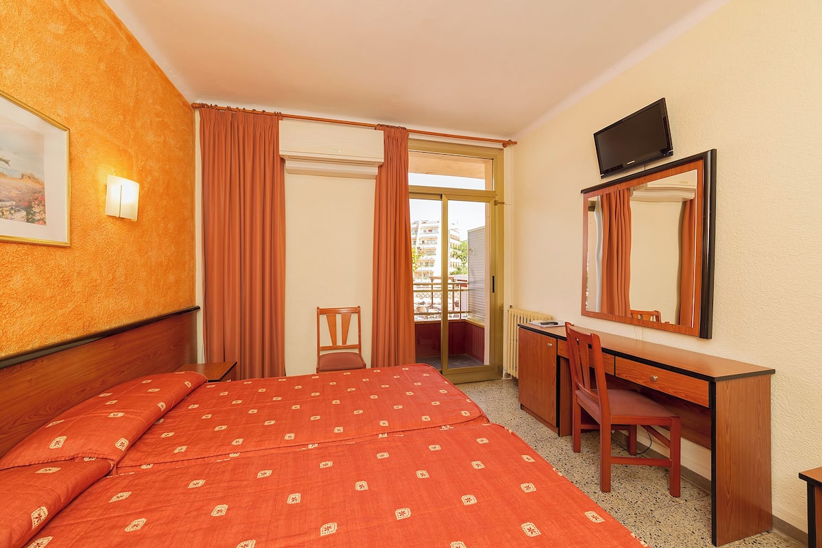 A hotel room with a bed, a desk, a chair, a television, and a window with curtains.