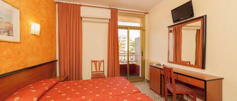 Habitación de hotel con cama, escritorio, silla, televisor y ventana con cortinas.