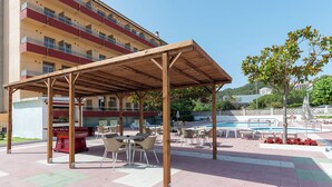 An outdoor patio area with a wooden pergola, seating, and a pool. - BLUESEA Continental (Tossa de Mar)
