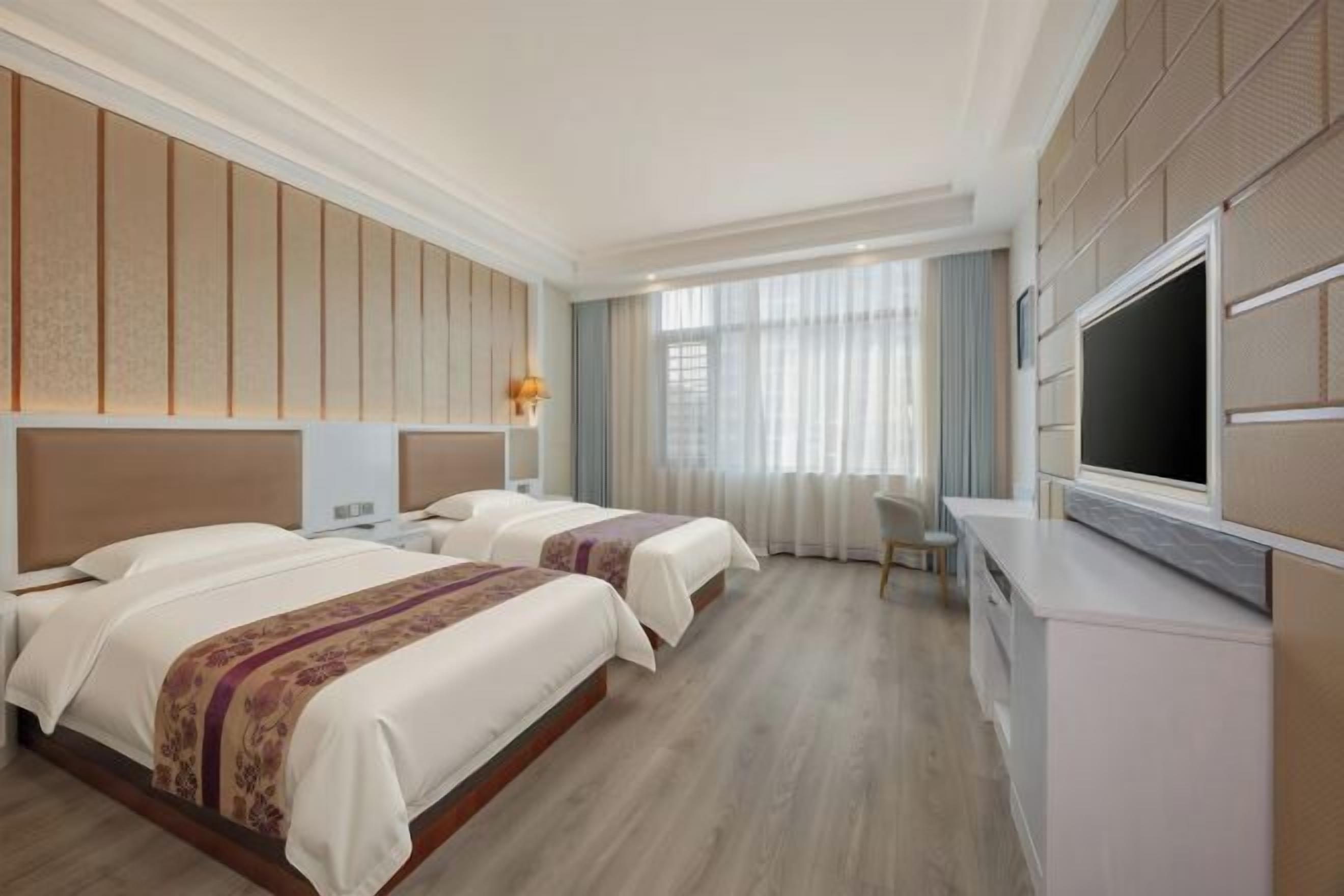 A hotel room with two beds, a flat-screen TV, a desk, and a large window.
