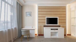 Une chambre d’hôtel moderne dotée d’un téléviseur à écran plat fixé au mur, d’un bureau blanc avec une chaise et d’une grande fenêtre avec des rideaux.