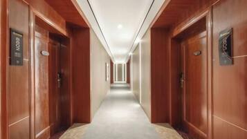 Un corridoio d'albergo con porte in legno, pavimento rivestito di moquette e soffitto con illuminazione a incasso.