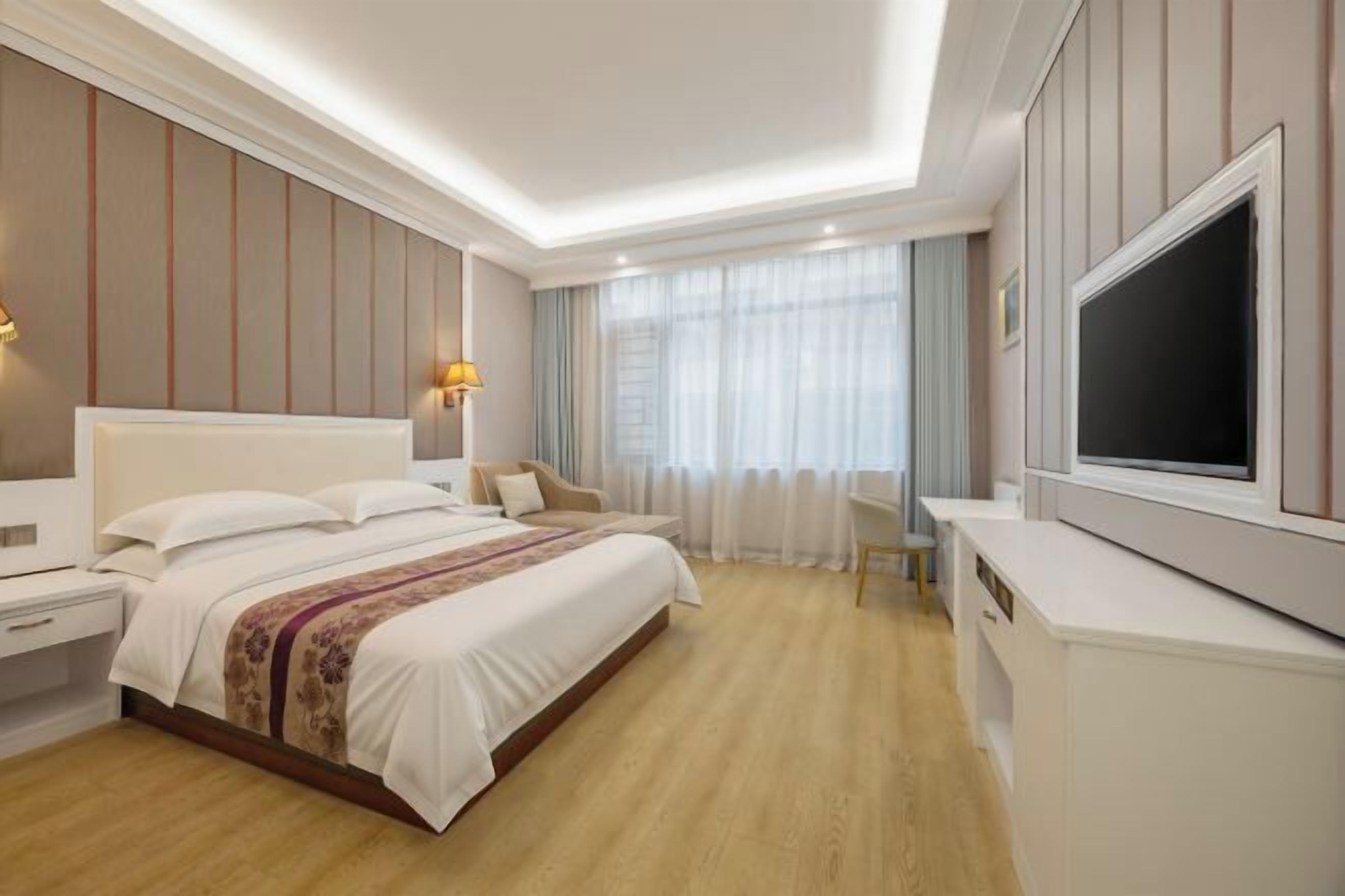 A hotel room with a large bed, bedside tables, a TV, and a desk.